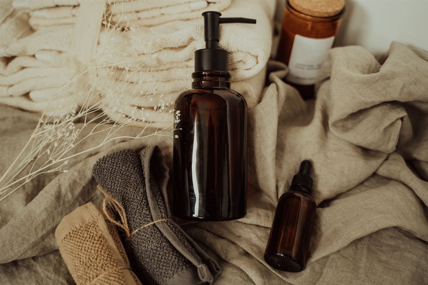 Frascos de skincare en vidrio ámbar sobre telas de lino en tonos naturales